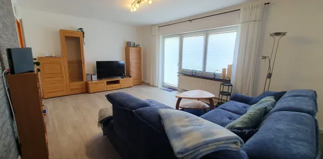 BookNoFees: aluguel de temporada em Langelsheim – Sala de estar com sofá azul, móveis de madeira e porta da varanda