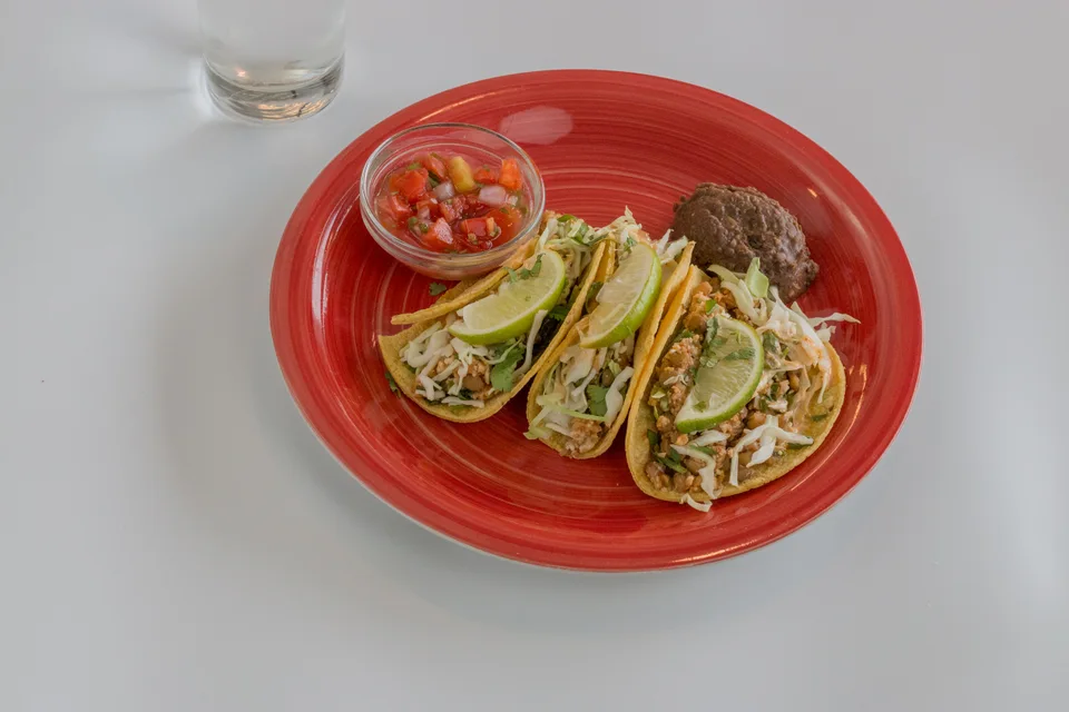 BookNoFees: Fotografia ilustrativa: Três tacos com rodelas de lima e molho num prato vermelho