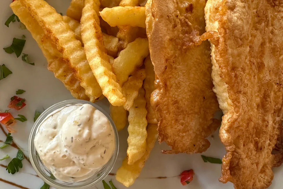 BookNoFees: Fotografia ilustrativa: Filetes de peixe envolvidos em polme com batatas fritas onduladas e uma pequena taça de molho