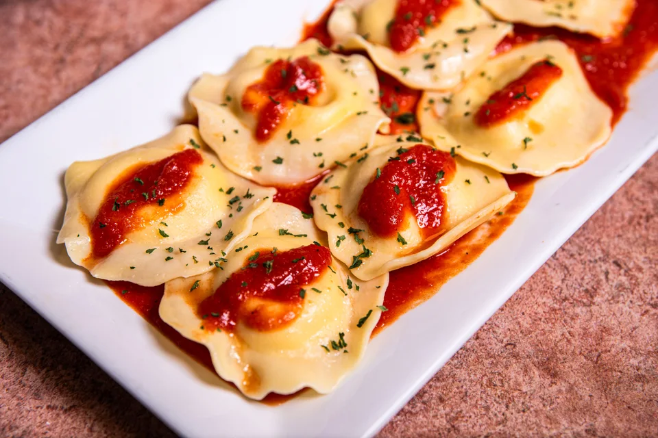 BookNoFees: Fotografia ilustrativa: Ravioli com molho de tomate e ervas aromáticas num prato branco
