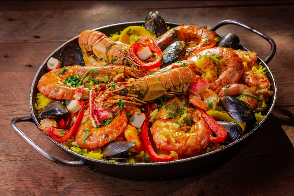 BookNoFees: Fotografia ilustrativa: Paella de marisco numa frigideira, coberta com marisco e pimento vermelho